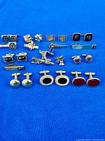 Overall view of cufflinks and tie clips laid out on blue cloth