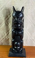 Front view of black carved totem pole replica on base