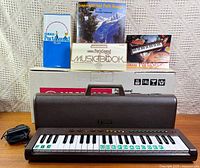 Keyboard in open case with accessories, box and books visible