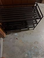 Front angled view of black 3-tier shoe rack showing slatted shelves and frame