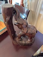 Full view of carved hardwood elephant interacting with tree