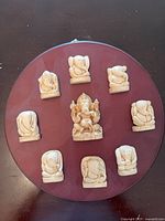 Front view of round maroon plaque with nine carved wood Ganesha figurines