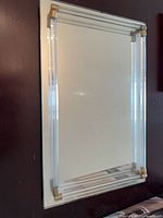 Frontal view of rectangular wall mirror with clear lucite rod frame and brass-tone corner mounts