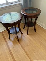 Two matching dark wood side tables with glass tops shown side by side