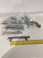 Group of bagged stainless steel cabinet pulls with one handle displayed and measuring tape showing length