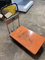 Full view of hydraulic lift table cart showing orange platform, handle, casters, and hydraulic unit