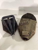 Folding entrenching tool next to canvas pouch