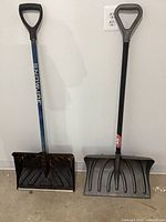 Two snow shovels standing against wall showing full items
