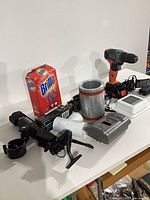 Group shot of all items including drill, alarm, Brillo box, scope, pipe parts, thermostat