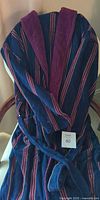 Full view of navy terry robe draped on chair showing stripes, collar, and sash belt
