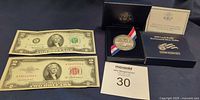 Overall lot showing coin in presentation box with certificate, two $2 bills