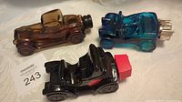 Three colored glass car-shaped Avon bottles on table with lot tag visible