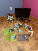 Overall lot showing Dell monitor with cables, game discs/cases, Guinness World Records 2023 book, manga volume, green thumb grips