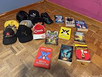 Group shot showing ten baseball caps and nine children’s books laid out on floor