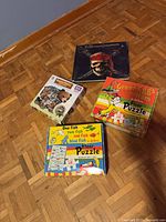 All four boxed items displayed on floor: two Dr. Seuss floor puzzles, animal-shaped 100-pc puzzle, Disney Pirates book/album