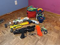 Overall lot view showing all four Nerf blasters, magazine, darts, goggles, fabric bin, toy workbench and pail