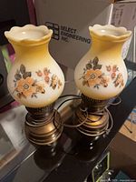 Both hurricane-style floral milk glass lamps showing shades and bases