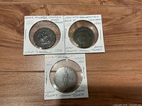 Obverse sides of three half penny tokens in cardboard 2x2 holders with handwritten labels