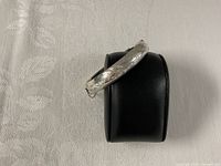 Side view of hinged sterling silver bangle on display stand showing engraved pattern