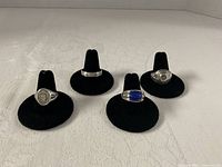 All four sterling silver rings displayed on black ring stands