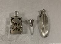 Three sterling vanity items lined up: overlay perfume bottle, petal funnel, fluted powder flask