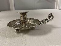 Side view showing hammered dish, candle socket, scroll handle, ball feet