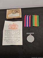 Medal, box with label, four ribbon lengths, condolence slip displayed on dark surface