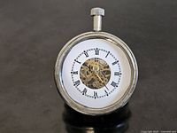 Front view of chrome-tone skeleton desk clock showing Roman numeral dial and exposed brass movement