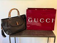 Front view of black calfskin tote beside red Gucci shopping bag