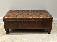 Full view of brown leather tufted storage ottoman on tiled floor