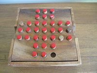 Top view of teak board with red and natural pegs arranged, empty starting hole visible
