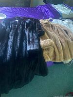 Both fur coats displayed side by side on bed