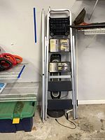 Stepladder folded against wall with fan base visible