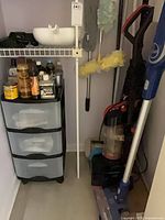 Closet showing both vacuums, drawer unit, dustpan and bottles