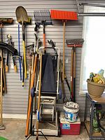 Group of long-handled yard tools, hose reel cart, paint buckets