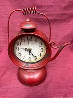 Front view of red metal teapot clock showing dial