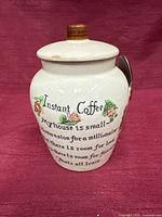 Front view of ceramic coffee canister showing printed text and floral design with lid on