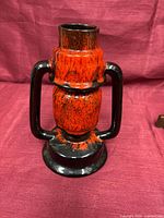 Front view of red-orange and black fat lava ceramic vase showing full shape and handles