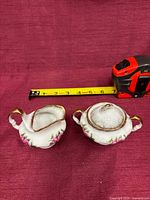 pair showing sugar bowl with lid and creamer beside tape measure