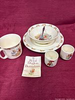 Full set displayed on cloth—mug, bowl on plate, two egg cups, fork, booklet