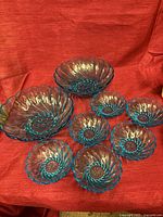 Full set of teal blue swirled glass bowls displayed on red fabric
