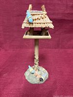 Full view of thatch-roof hut on pedestal with birds at base