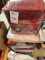 Stack showing burgundy blanket in packaging, sealed white pad, boxed blanket, used folded blanket