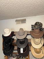 Front view of hat rack showing multiple western hats, white fedora and stacked bucket hats