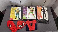 All four costumes laid out: two sealed TMNT kits, sealed black cat jumpsuit kit, Spider-Man pieces