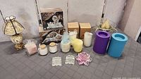 All items arranged on table showing variety of candles, holders, lamp and boxed items