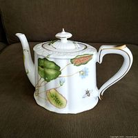 Left-side view showing floral and insect design, gold trim, sculpted lid