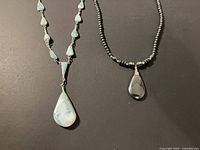 Both necklaces side by side on black surface showing overall design and pendants