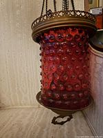 Full view of cranberry hobnail glass shade with brass crown and chains