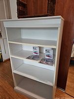 White bookshelf with items on shelves, wood/wicker unit partially visible